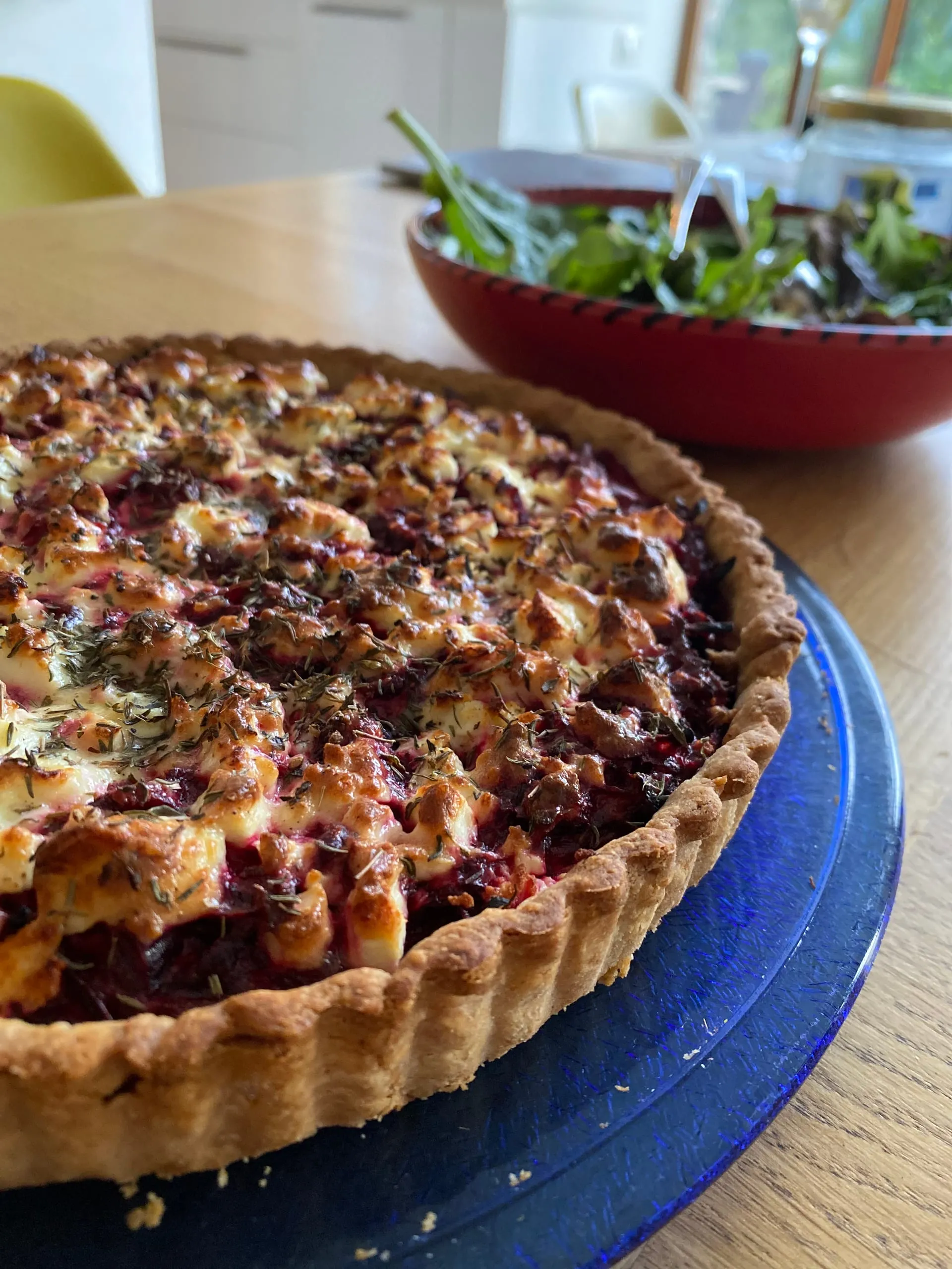 Une tarte à la betterave et au chèvre parsemée de thym, un saladier derrière elle