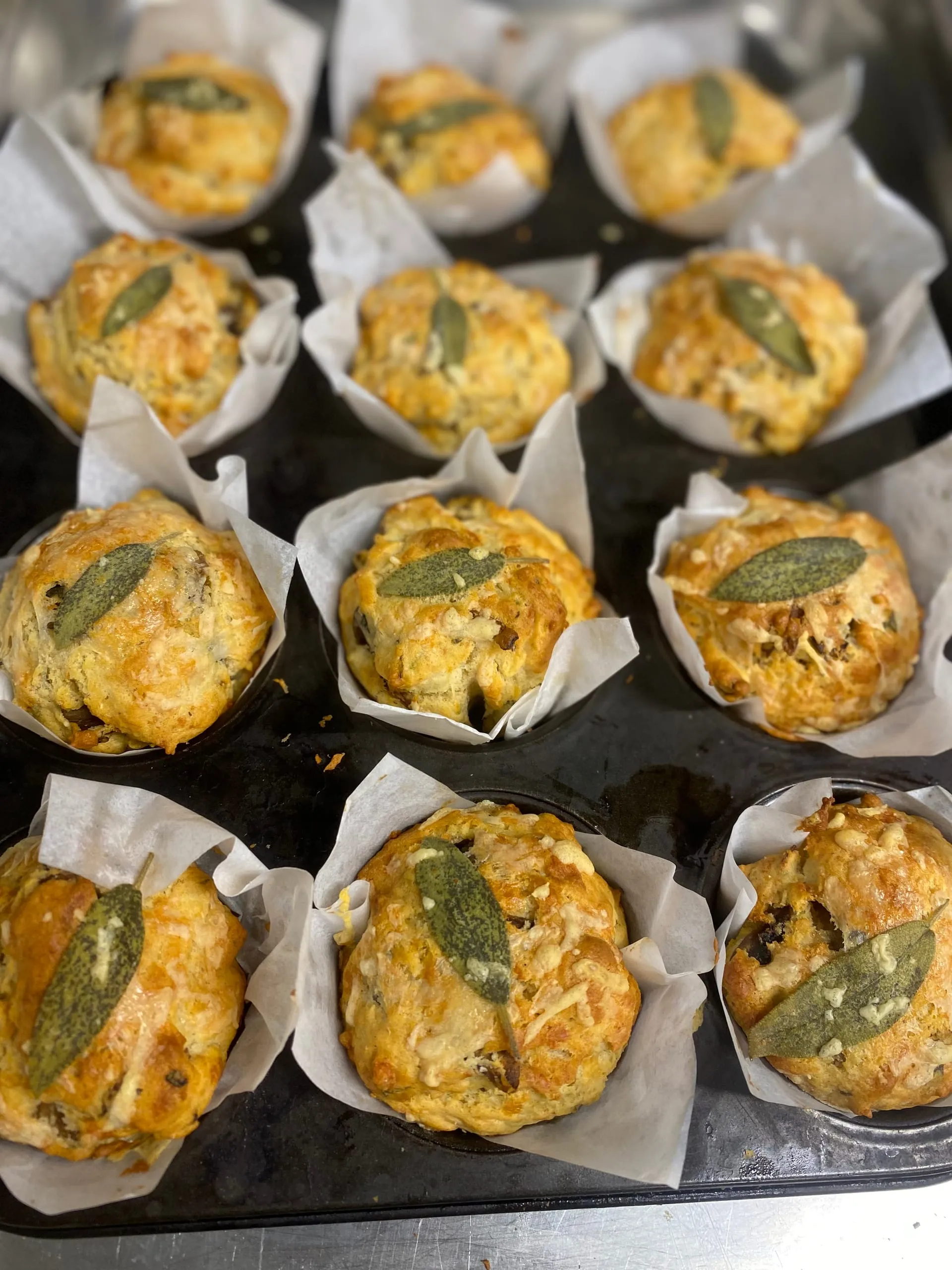 Des muffins au fromage et à la sauge dans leur moule, une feuille de sauge cuite sur chacun