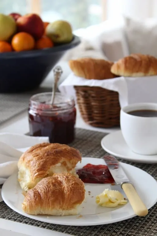 Des croissants frais servis au petit-déjeuner, avec un pot de confiture et une tasse de café