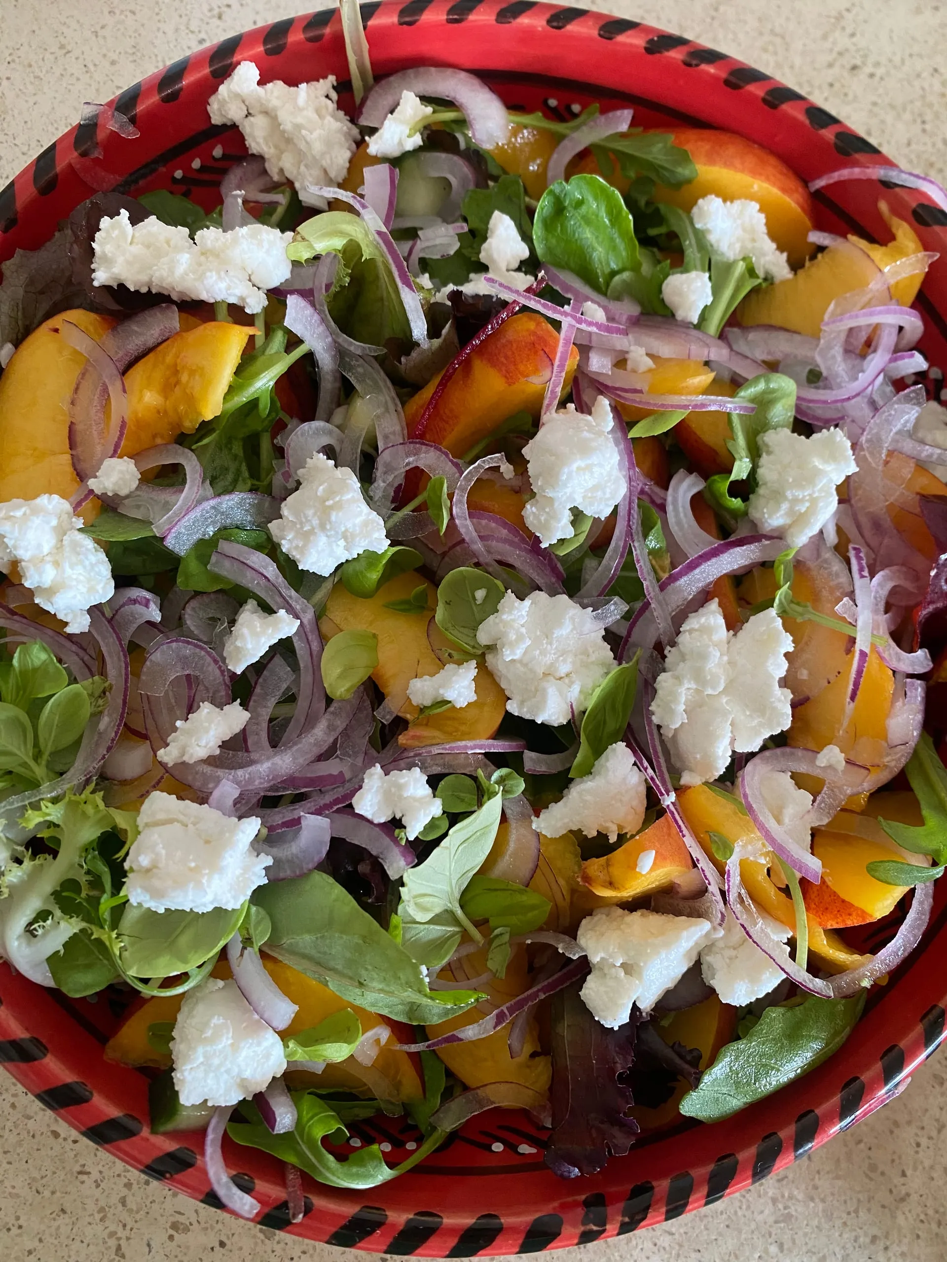 Une salade de pêches, de fromage de chèvre émietté, d’oignon rouge et de jeunes pousses